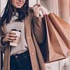 Woman holding coffee cup and walking near mall with shopping bags.