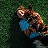 Smiling young woman holding her puppy on the green grass