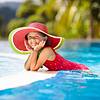 Little girl wearing red swimsuit and watermelon sun hat playing in outdoor pool