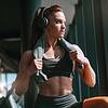 Muscular female with ponytail and headphones in gym with towel around neck