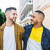 LGBTQ+ male couple walking along the street and looking at each other
