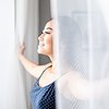 Woman opening windows and smiling in sunlight





