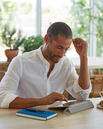Cafe Man sitting at cafe bar with cup of coffee working on tablet computer