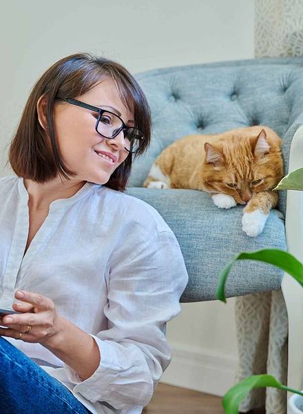 Woman on laptop next to cat in chair